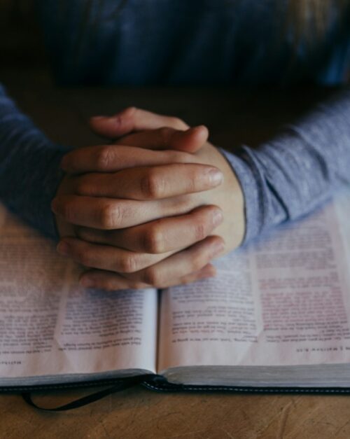 Clasped hands in prayer over open Bible